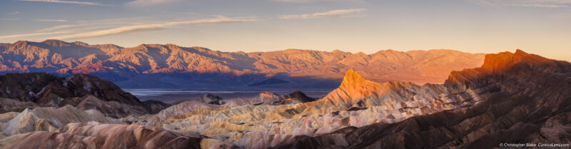 Panoramic view of Zabriskie Point at sunrise with the Panamint Mountains lit by morning light, highlighting the colorful and textured badlands of Death Valley.