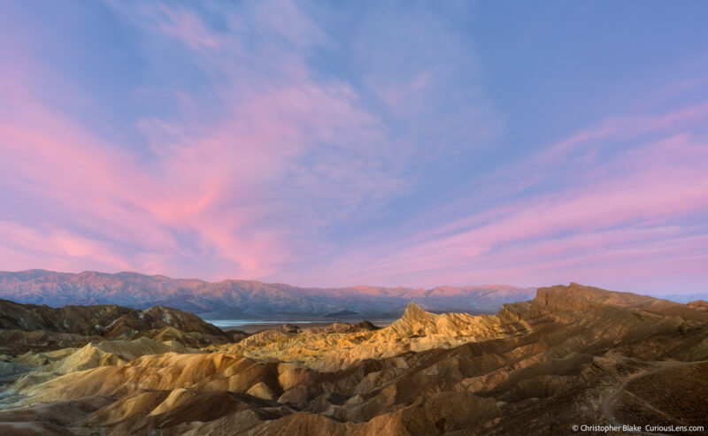 Sunrise over Zabriskie Point in Death Valley, showcasing vibrant red clouds above the textured badlands with the Panamint Mountains in the distance.