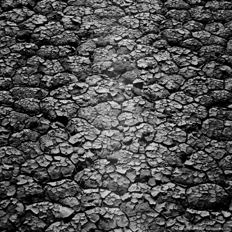 Close-up black and white image of the deeply cracked mud at Racetrack Playa, showcasing the unique texture created by extreme dryness.