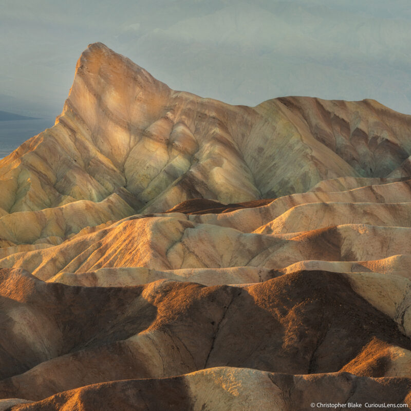 Close-up view of Zabriskie Point at sunrise, with warm yellow sunlight illuminating the textured rock formations of the badlands.