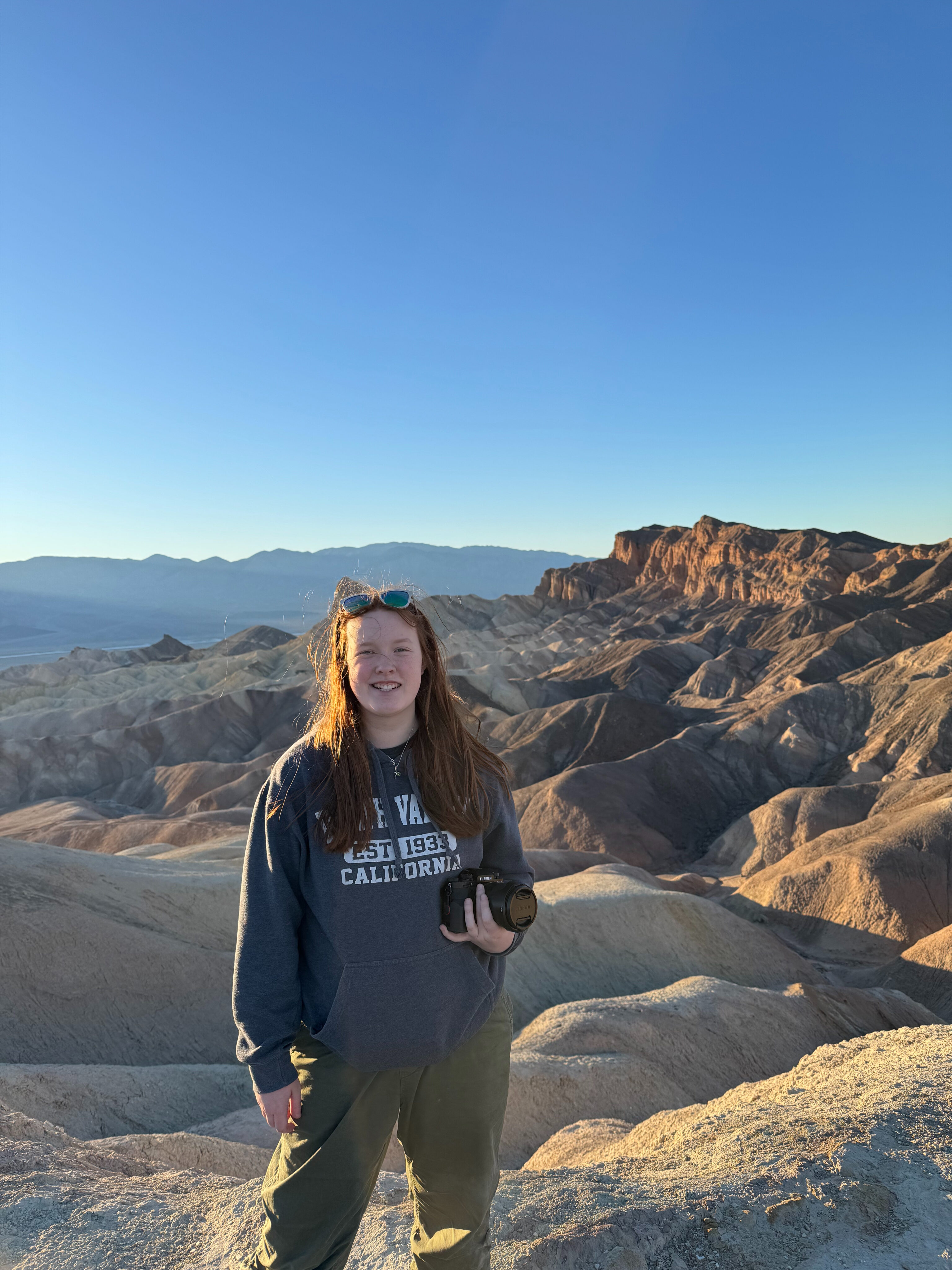 Cameron standing on top of the badlands at Zabriskie Point just after sunrise with her red hair blowing in the wind.