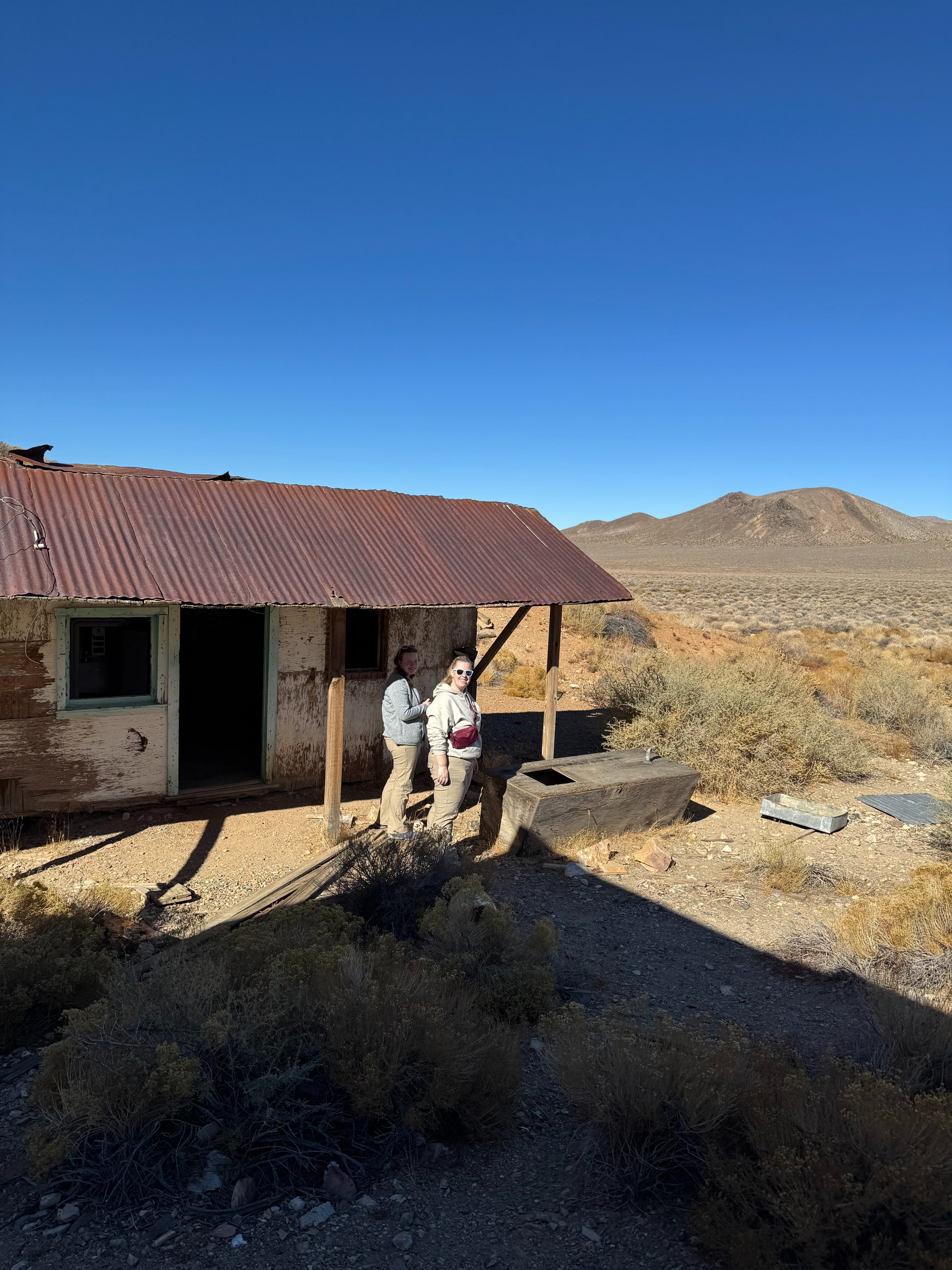 Cat and Cameron standing in front of one of the old buildings in the ghost town of Harrisburg in Death Valley.