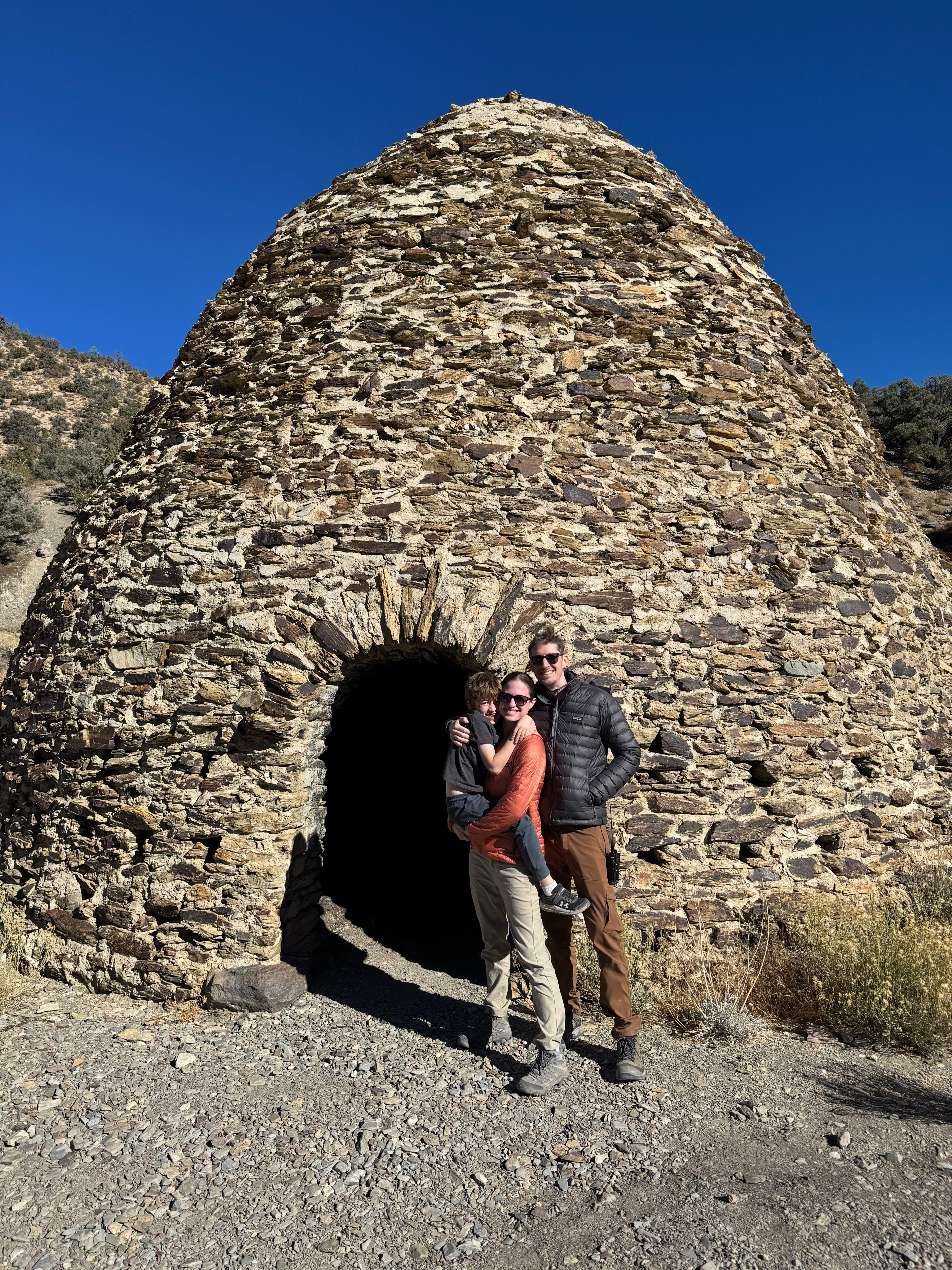 Aaron, Veronica and Nate standing in front of one of the wildrose Charcoal Kilns on a bright blue sky day in Death Valley.