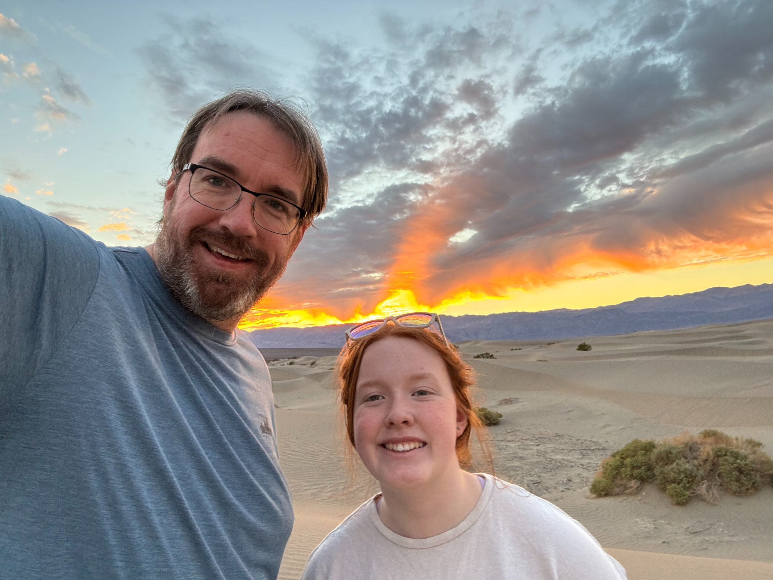 Chris and Cami on the Mesquite Dunes in Death Valley at sunset with a red sky and clouds above us.