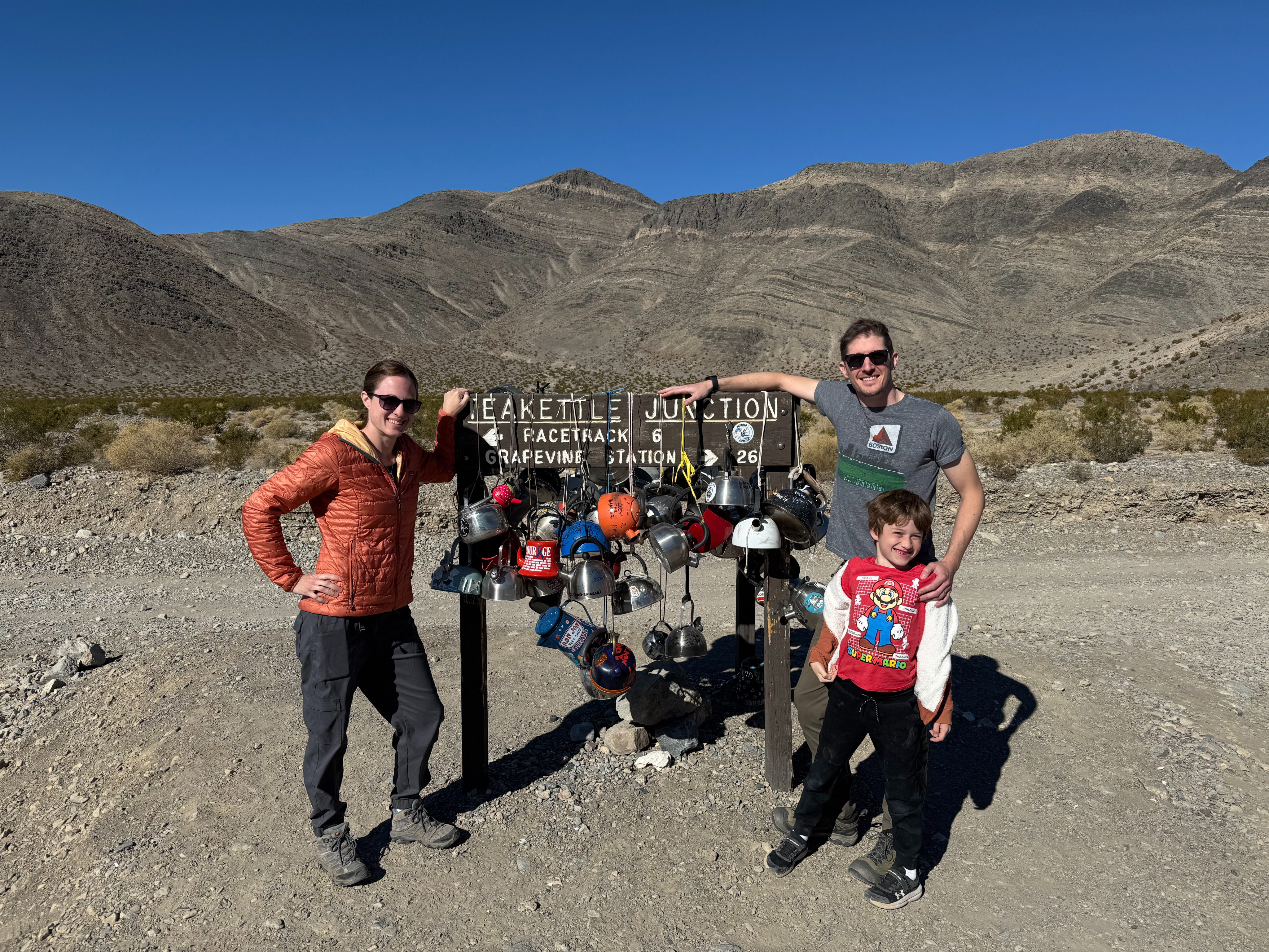 Aaron, Veronica, and Nate, standing in front of the sign for Teakettle Junction in Death Valley.