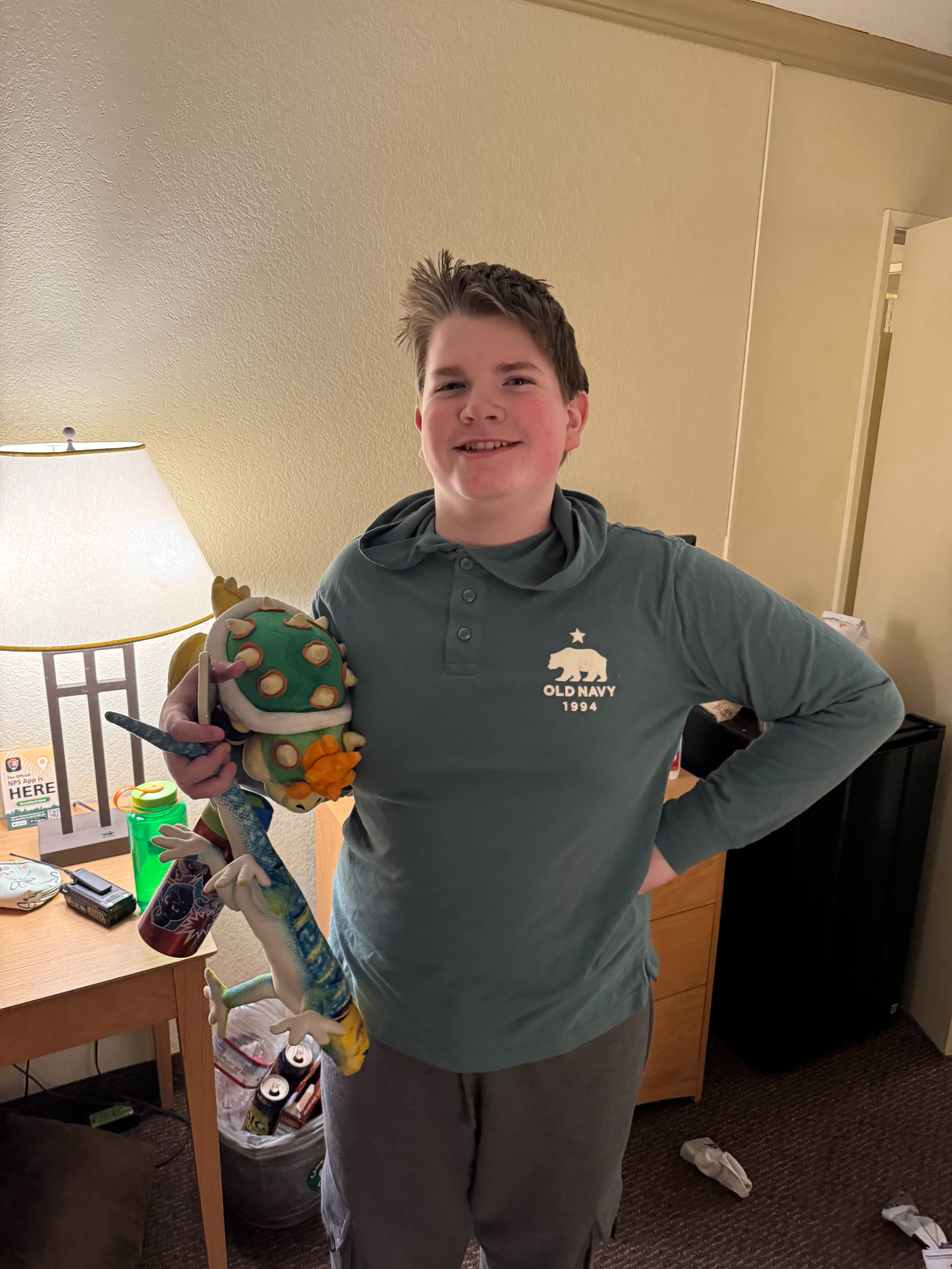 Collin standing in the hotel room with a big smile on his face holding his stuffed animals. 