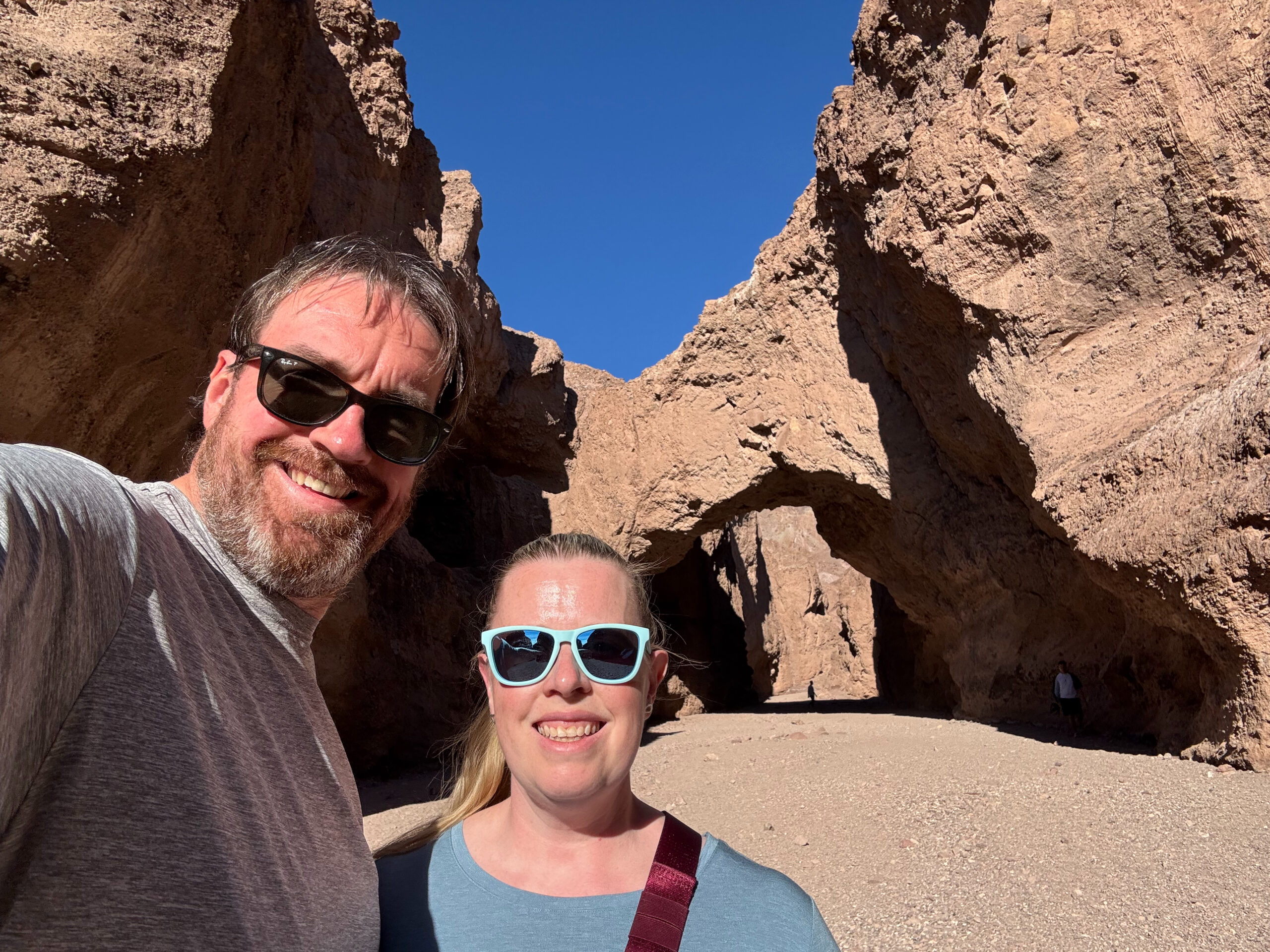 Chris and Cat standing wearing sunglasses at the end of the trail to the Natural Bridge with the rock formation behind us.