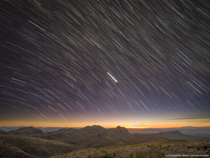 Long exposure photograph of star trails over the rolling hills of Big Bend National Park at twilight, showing a smooth transition from sunset to starry night.