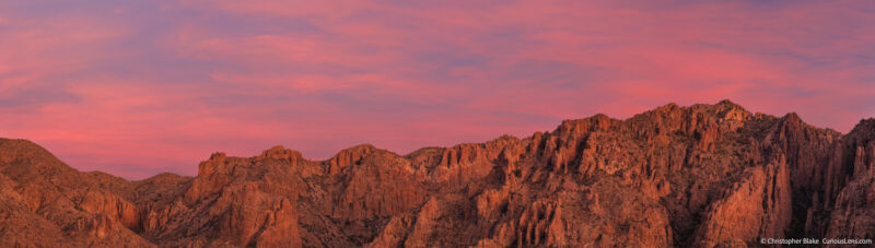 Panoramic view of the Chisos Mountains at sunrise in Big Bend National Park, showcasing sharp mountain ridges against a vivid red sky.