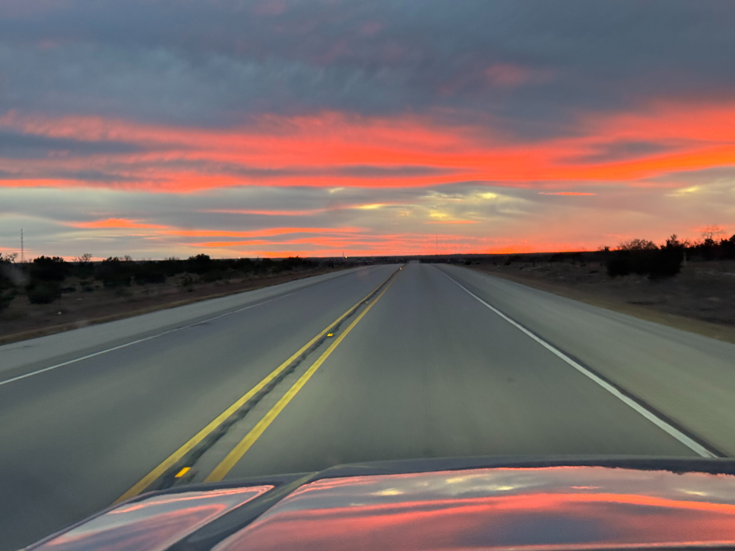 A view out the windshield driving through West Texas of a stunning red sunset. 