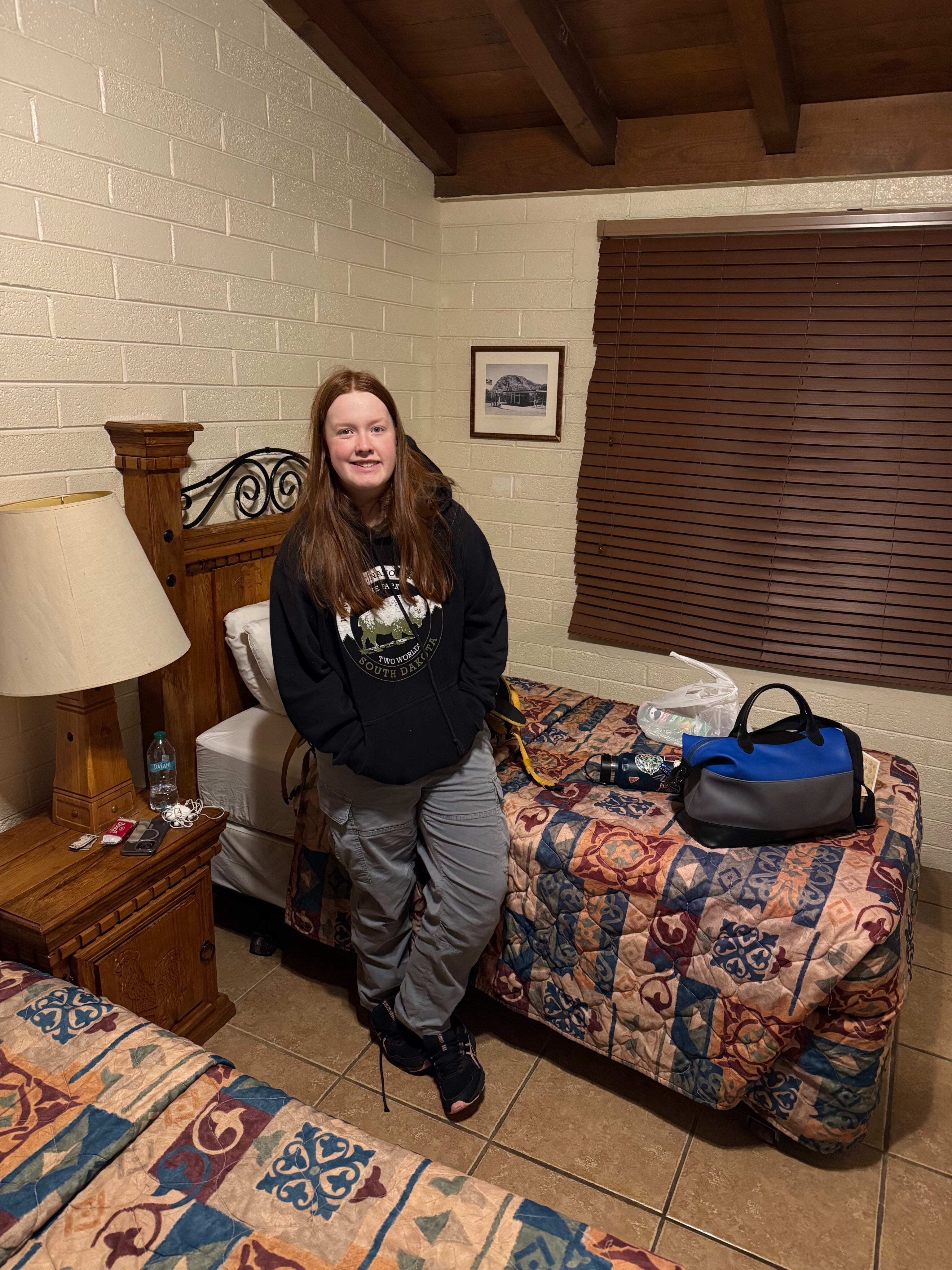 Cami standing by her bed in the Chisos Mountains Lodge after a long day of driving. 
