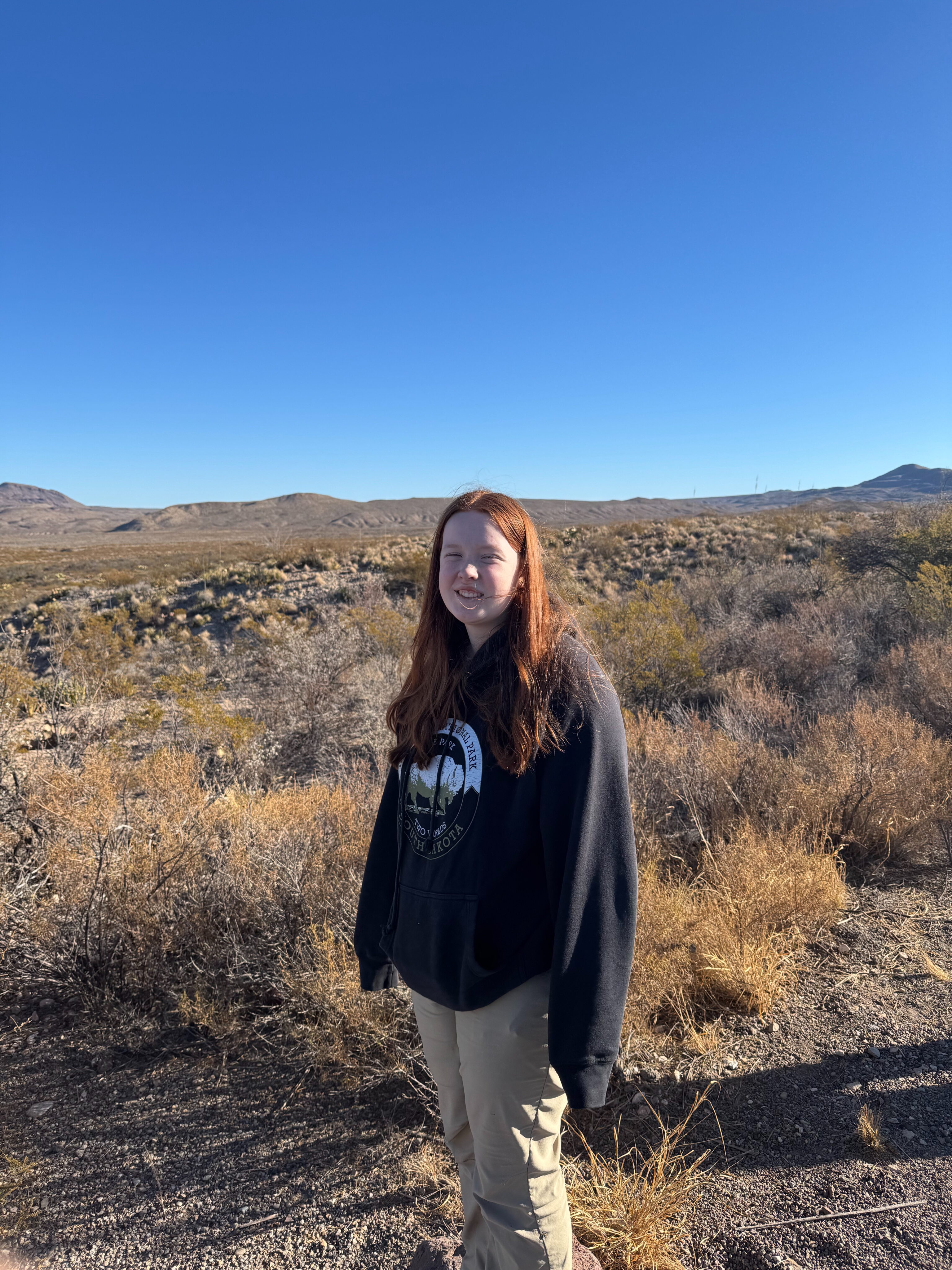 Cameron in a sweatshirt standing in the desert on a blue sky day off the Ross Maxwell Scenic Dr.