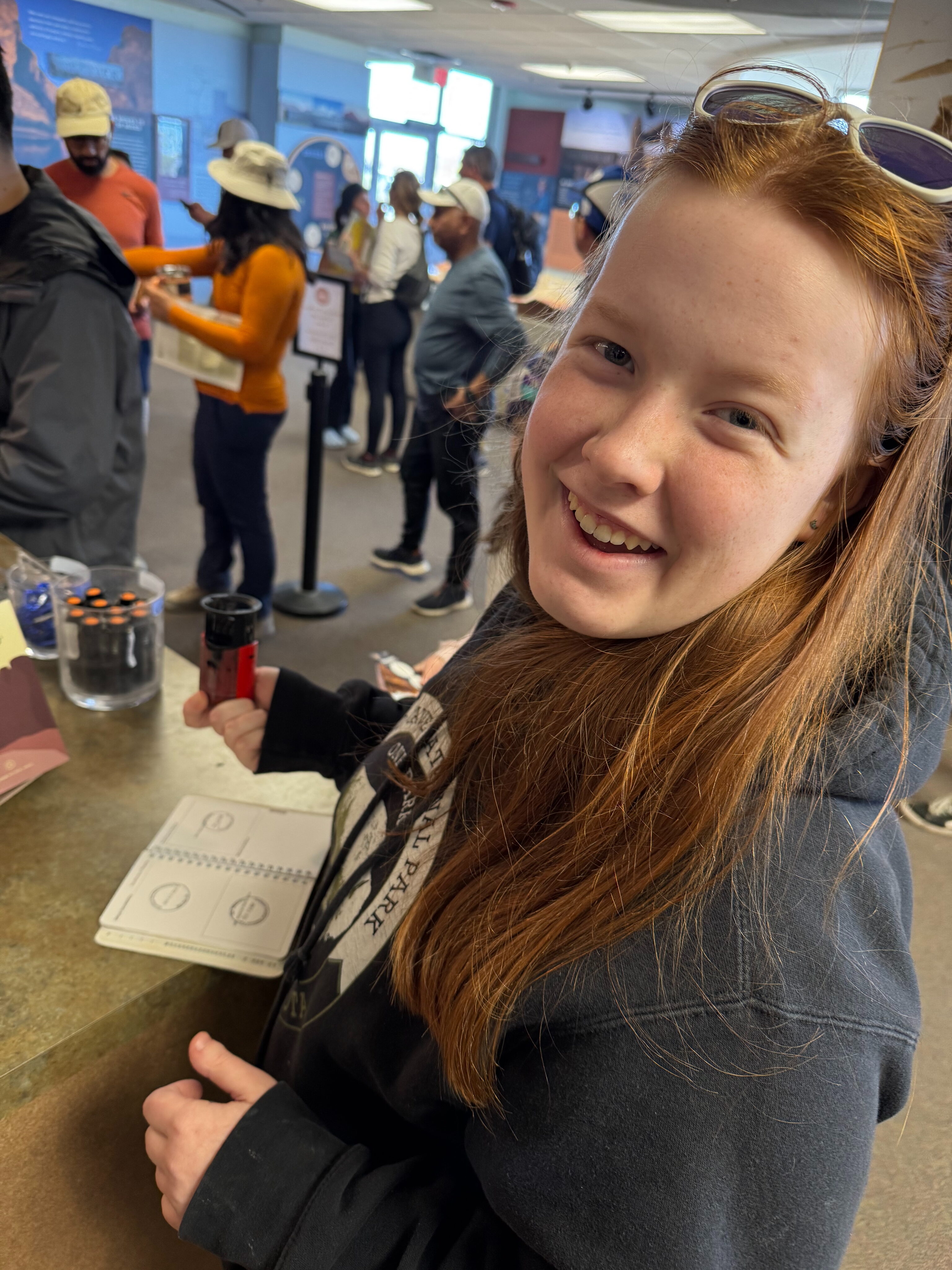 Cameron with sunglasses on top of her head, smiles as she stamps her National Park passport book in the Big Bend visitors center.