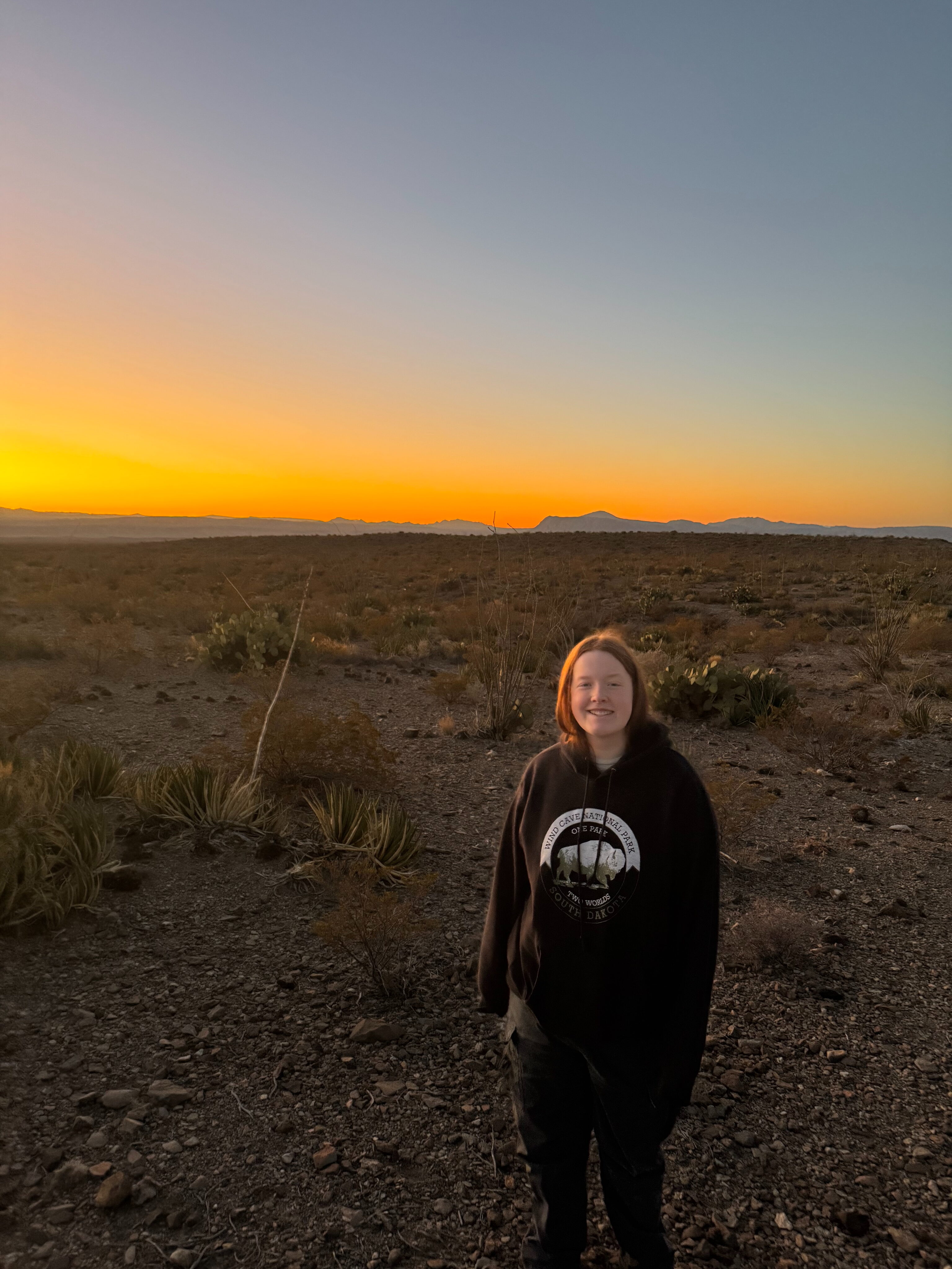 Cameron standing in the dark desert as the last light of day falls away and the sky turns orange. 