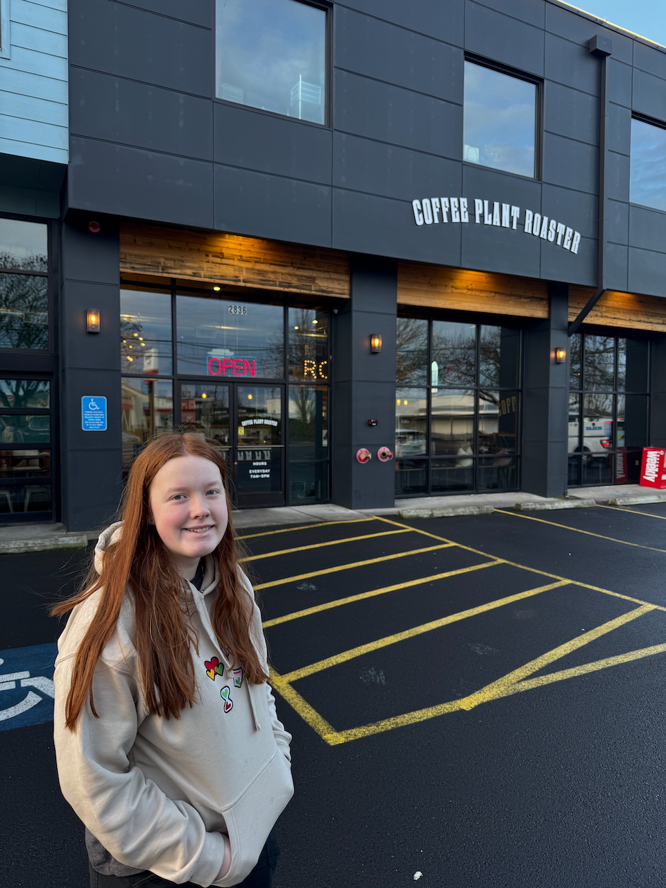 Cameron in her hoodie standing in a wet parking lot with a smile in front of the Coffee Plant Roaster before breakfast.