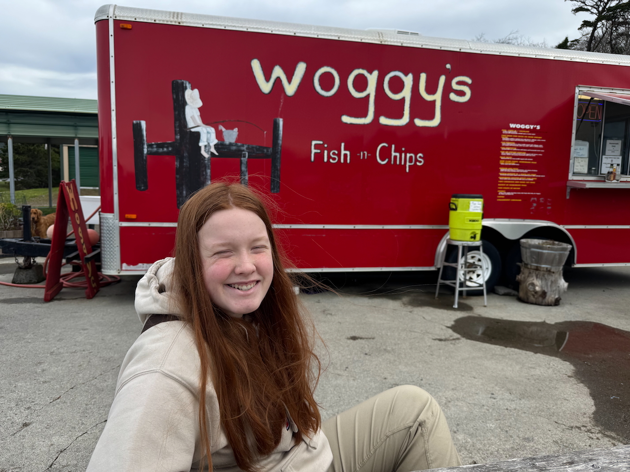 Cameron with a big smile sitting on a table in front of the Woggys Fish and Chip food truck in Gold Beach OR.