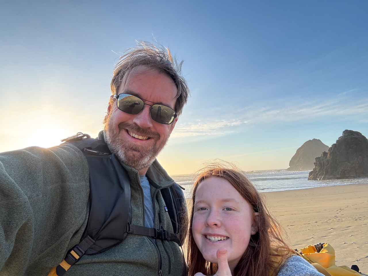 Cameron and myself standing on the sand taking a selfie with big smiles at sunset on Ariya's Beach. With a golden sunset just starting behind us.