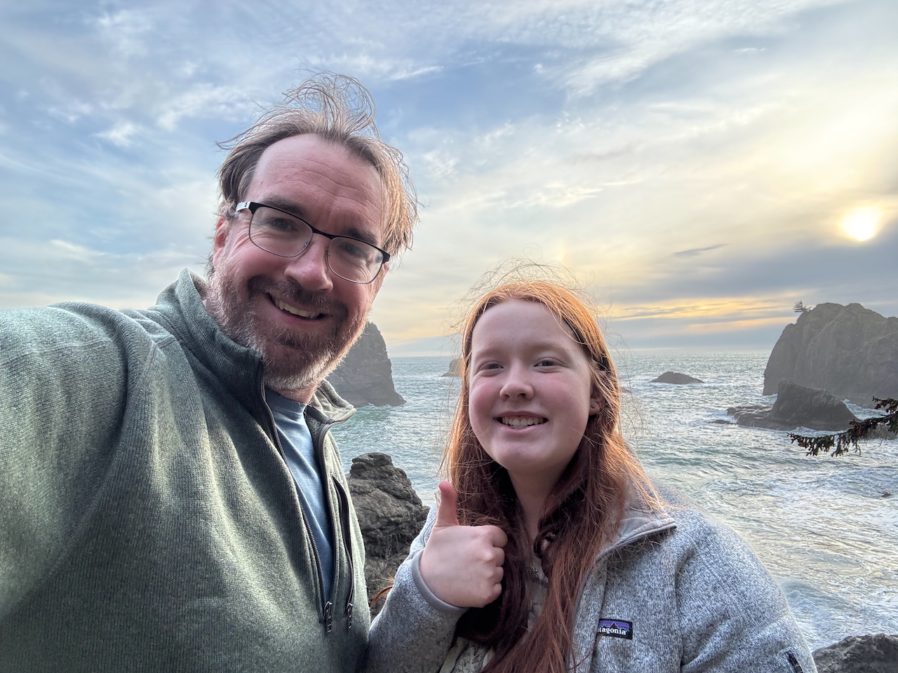 Cameron and myself with big smiles and her giving a thumbs up at secret beach with the ocean behind us at sunset.