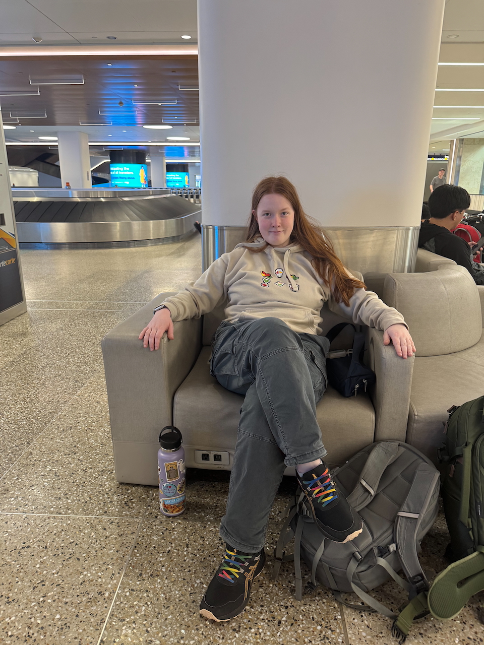 Cameron sitting in a chair, with her legs crossed waiting for our bags at arrivals at the MSP airport.
