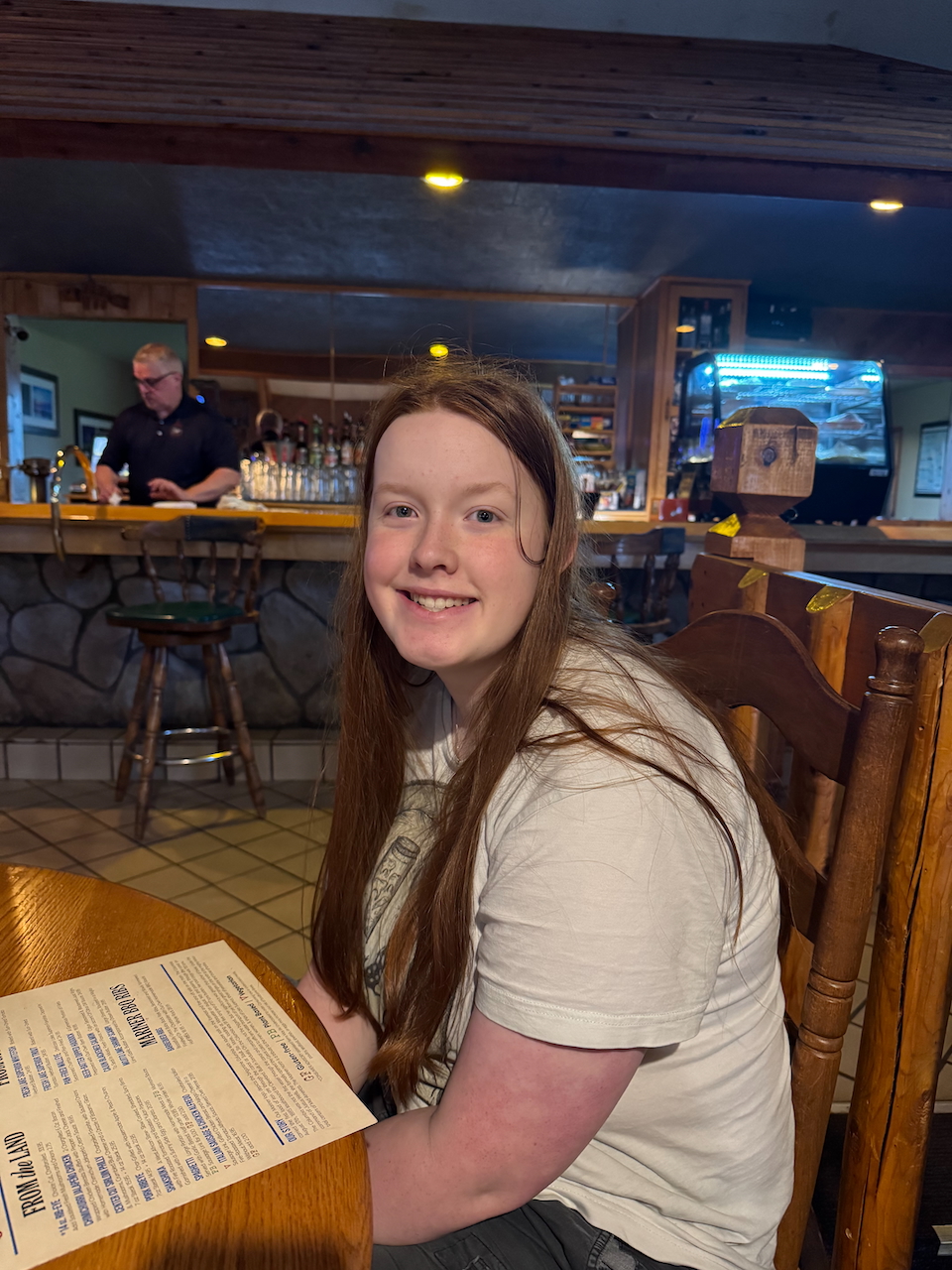 Cameron sitting on a wooden chair at The Mariner North waiting to order our late night dinner in Copper Harbor.