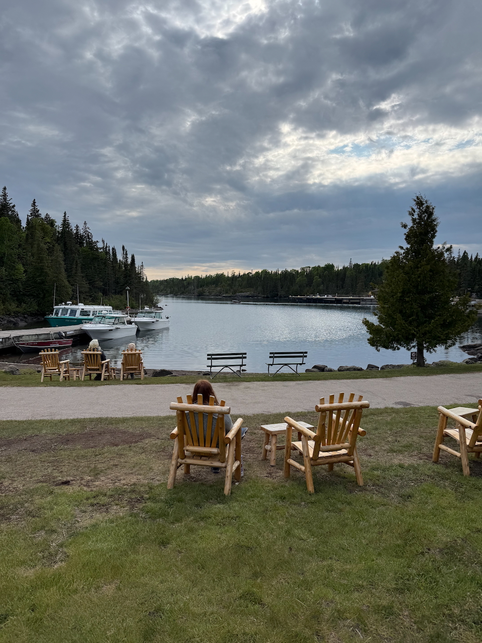 Cameron looking over Rock Harbor from a rustic chair with clouds in the sky and some boats docked.