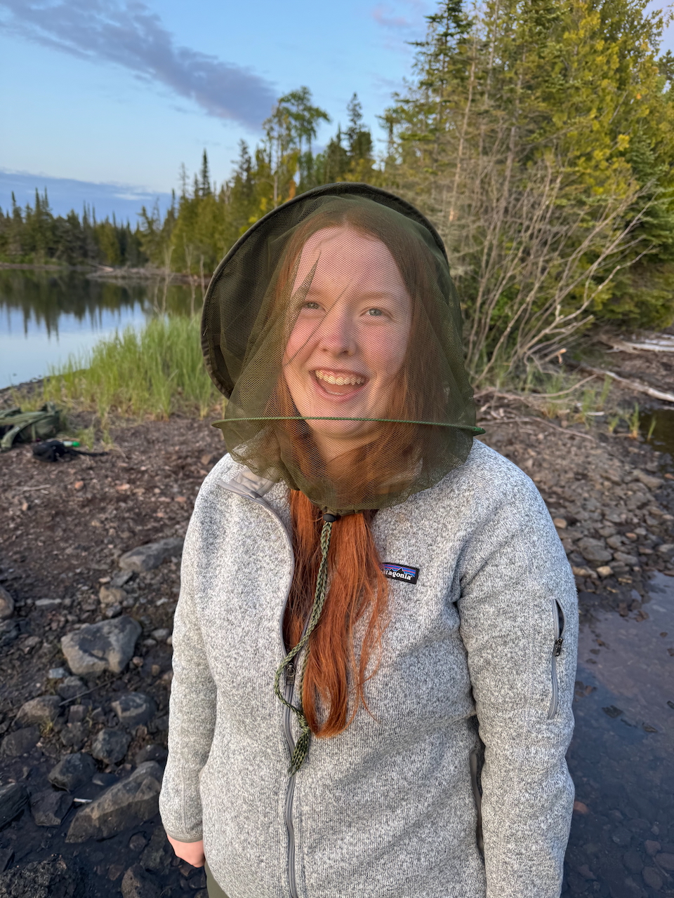Cameron with a big funny smile on her face as she poses for a photo on the trail in Isle Royale - wearing a headnet.