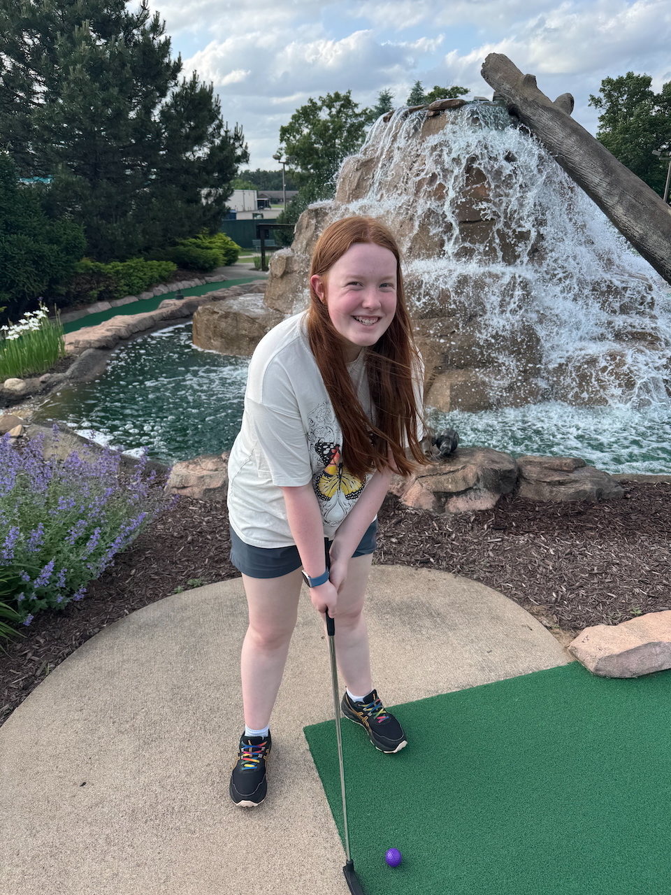 Cameron about to swing playing mini golf at Sawmill Adventure Park with a massive water feature behind her.