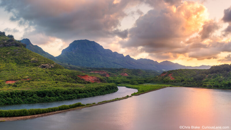 Sunset over Alekoko Fishpond with mountains and glowing clouds reflected in calm waters, Kauai, Hawaii.