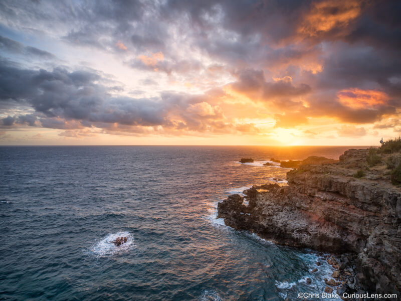 Golden sunrise at Nakalele Blowhole on Maui with storm clouds breaking over the Pacific Ocean and light reflecting on the waves.