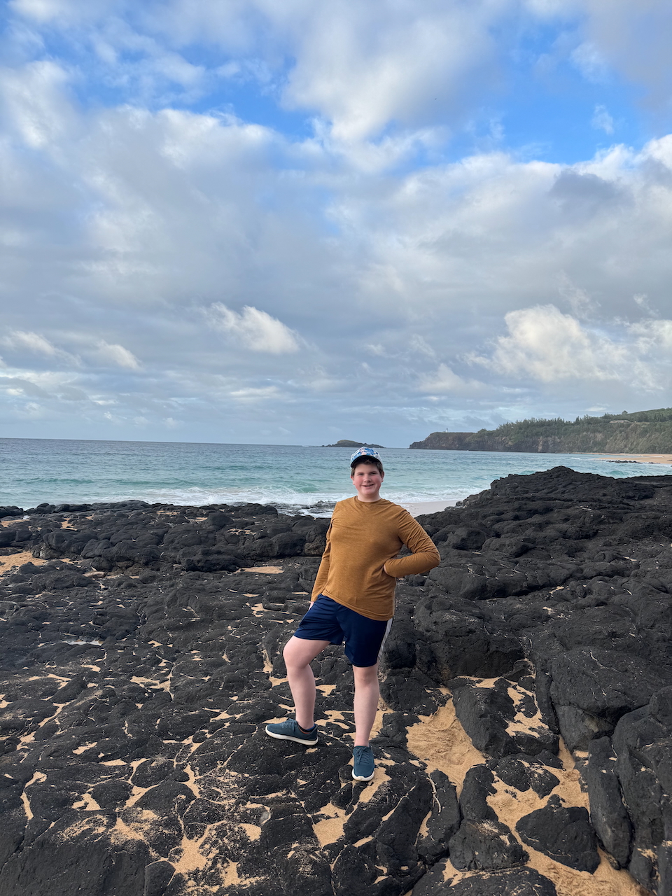 Collin standing on lava rocks at Secret Beach with the ocean behind him.
