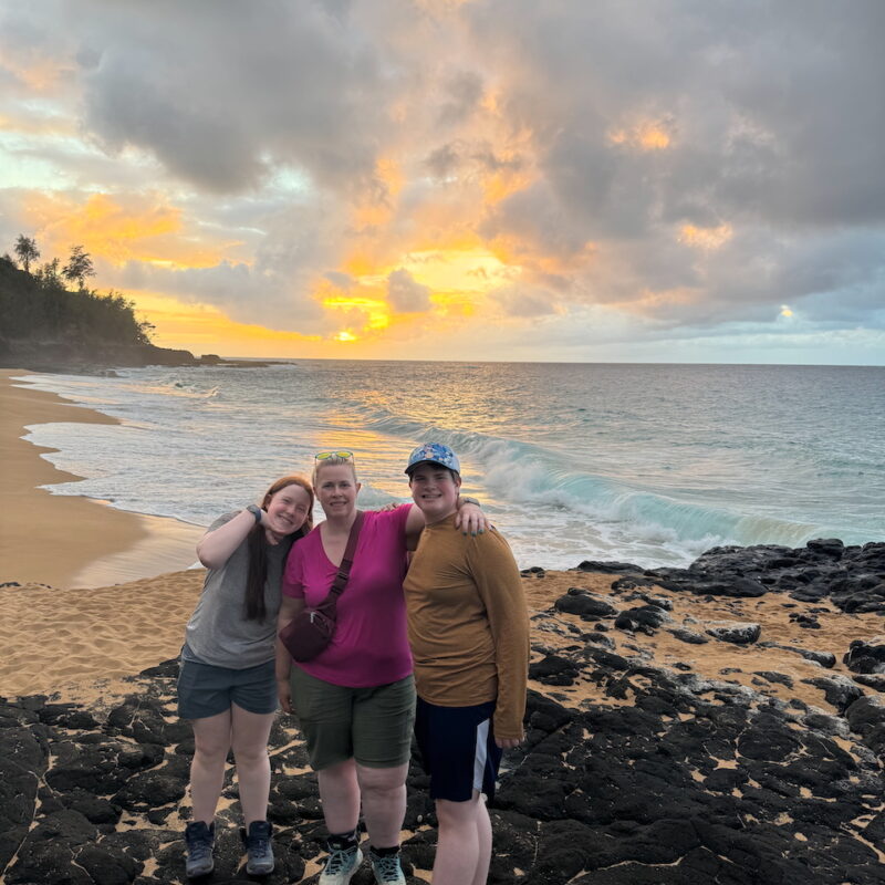 Cat, Collin, and Cameron smiling on the lava rocks at Secret Beach.