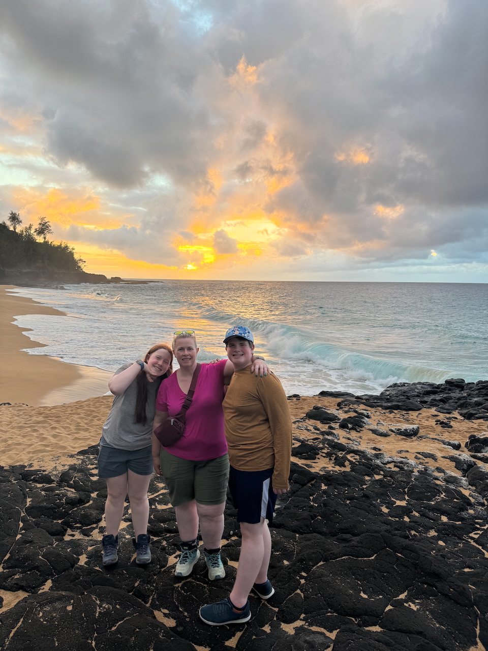 Cat, Collin, and Cameron smiling on the lava rocks at Secret Beach.