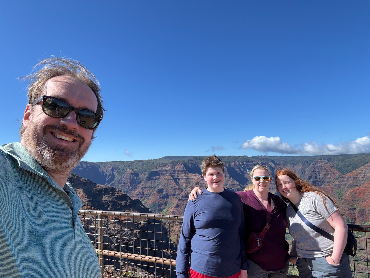 Family group photo at Waimea Canyon Lookout, overlooking the canyon walls and ridges.