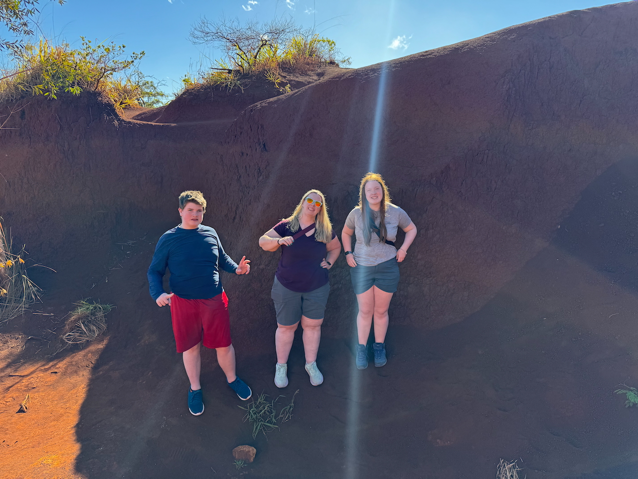 at, Collin, and Cameron hiking on the red dirt trail near Waimea Canyon Lookout.