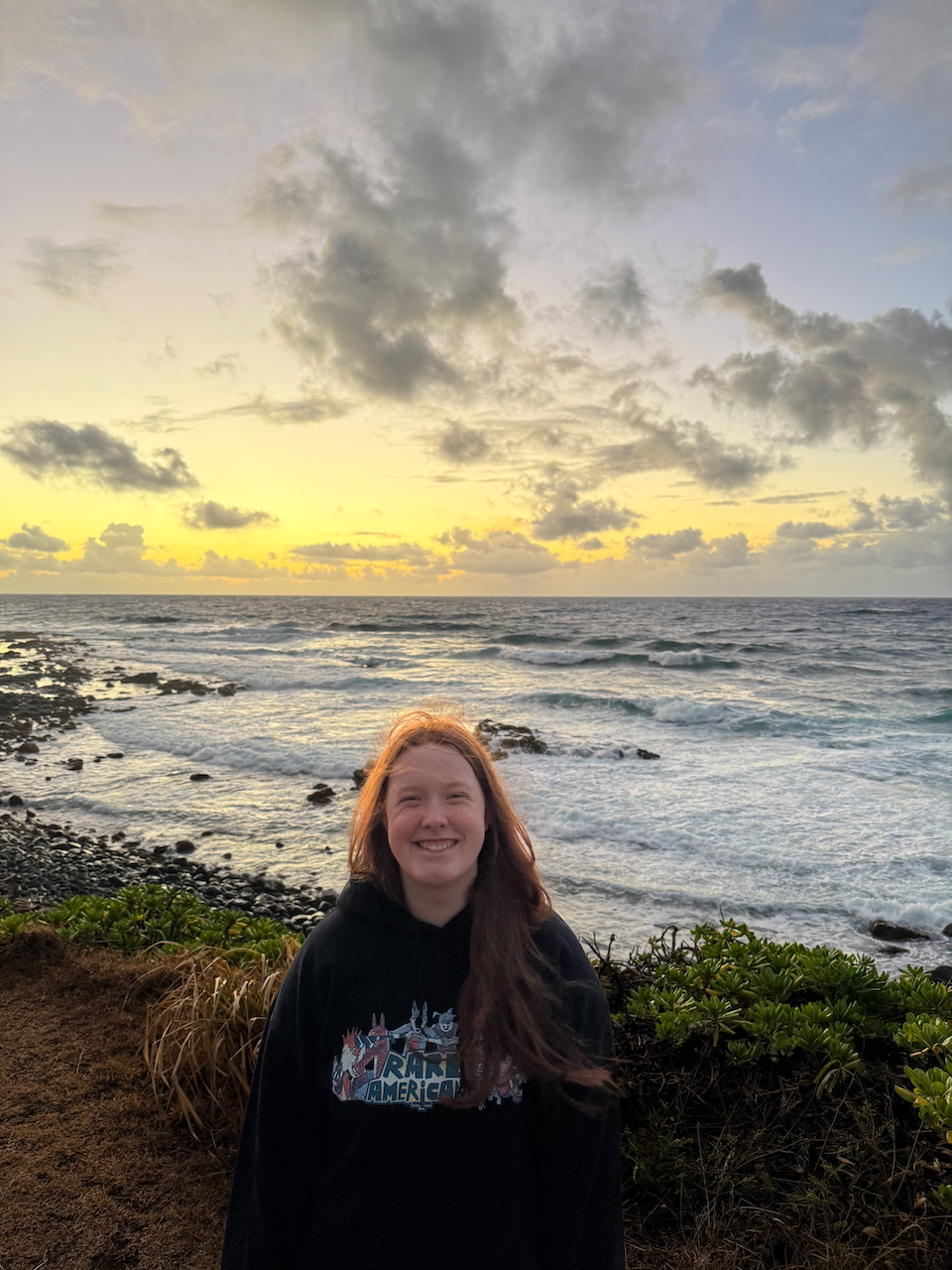 Cameron standing near the shoreline at sunrise with golden light reflecting on the waves.