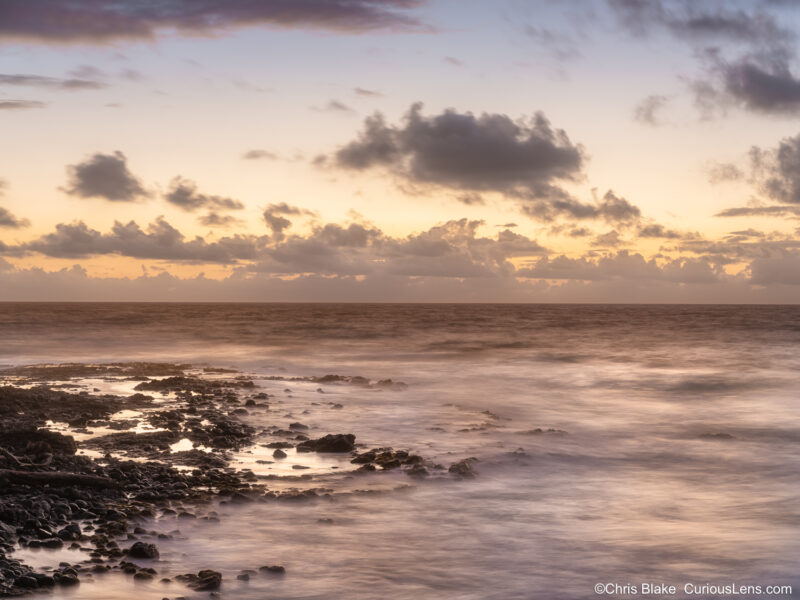 Sunrise along Ke Ala Hele Makalae on Kauai, with tidepools and shoreline rocks reflecting morning light.
