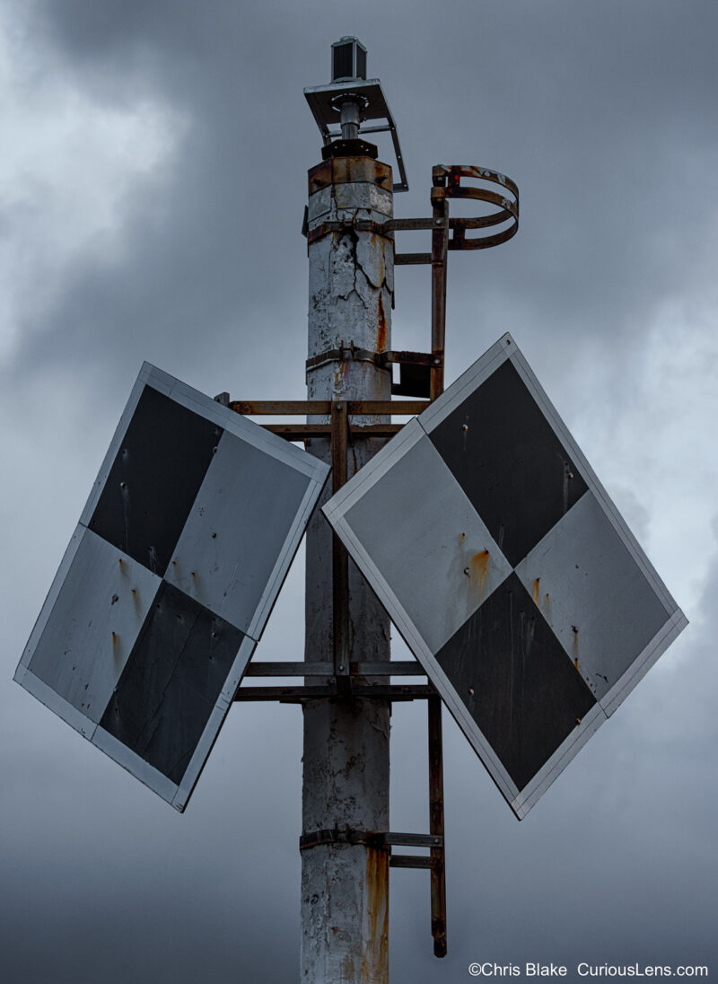 Close-up of rusted lighthouse marker at Nakalele Blowhole with storm clouds behind.