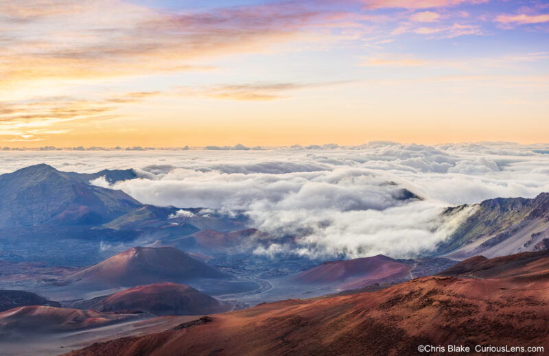 Panoramic sunrise above the clouds at Haleakalā Crater with cinder cones, volcanic ridges, and morning light on the landscape.