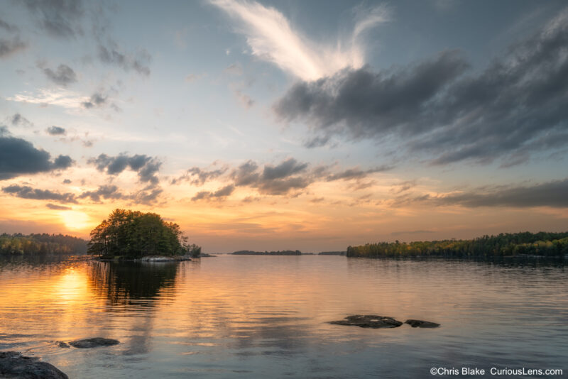 A small forested island on Kabetogama Lake glows in the warm light of sunset, reflecting across the calm northern waters of Voyageurs National Park.