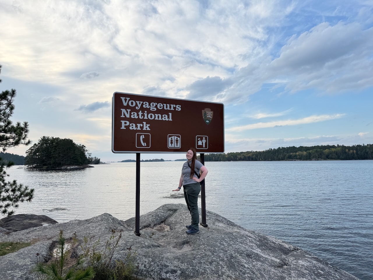 Cameron standing beside the Voyageurs National Park sign on the shore of Ash River — the only park sign located directly on the water.
