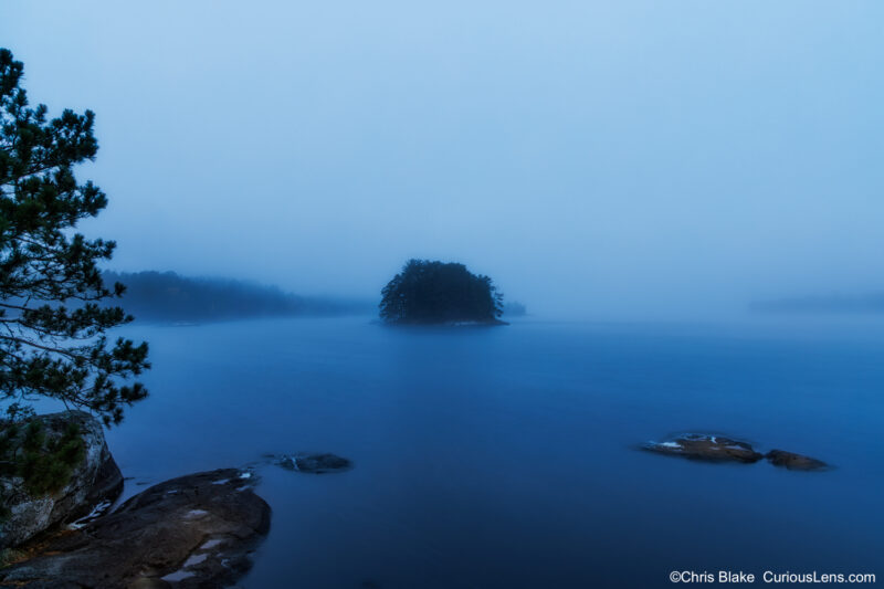 A small pine-covered islet surrounded by fog during blue hour on Kabetogama Lake in Voyageurs National Park, Minnesota.