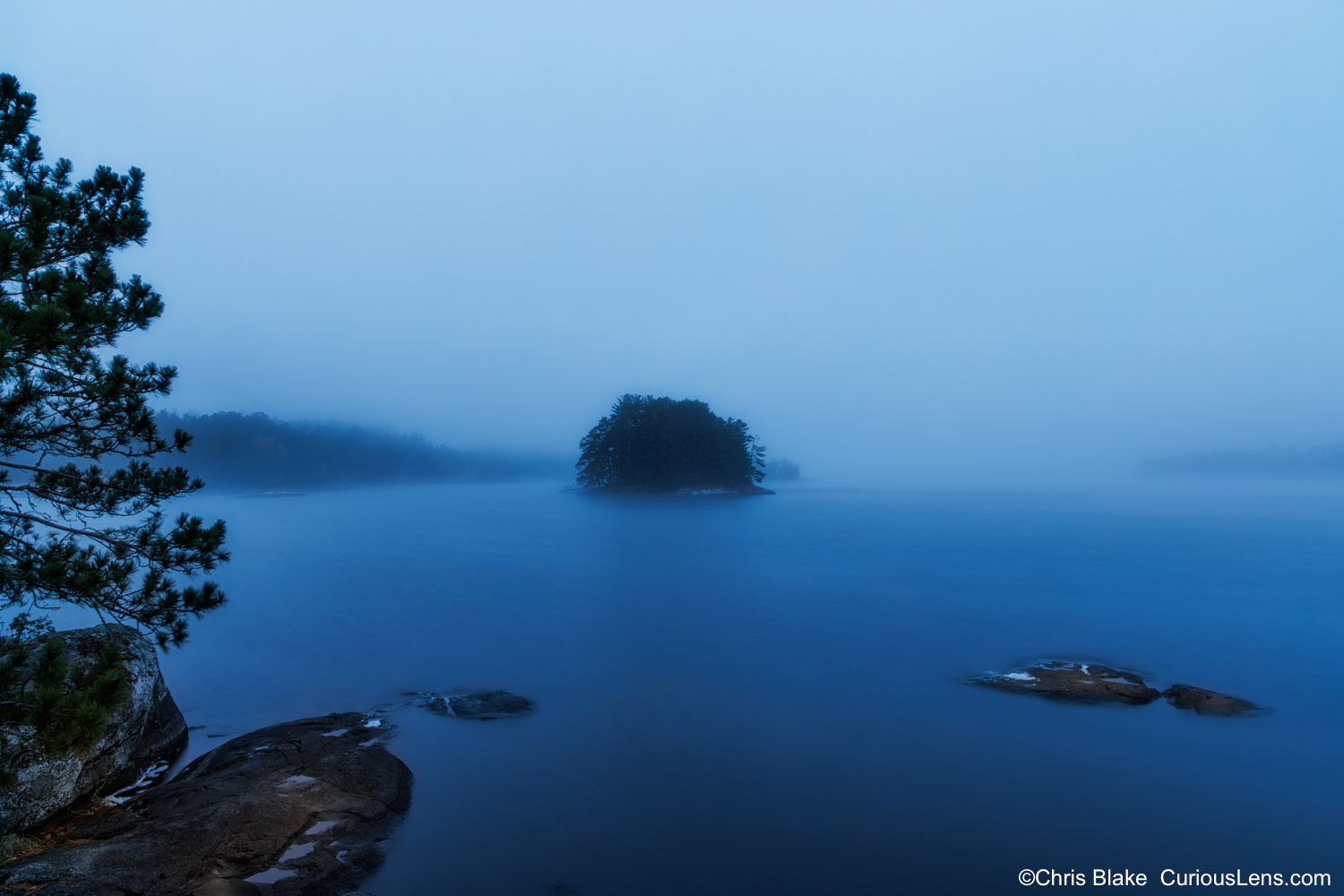 A small pine-covered islet surrounded by fog during blue hour on Kabetogama Lake in Voyageurs National Park, Minnesota.