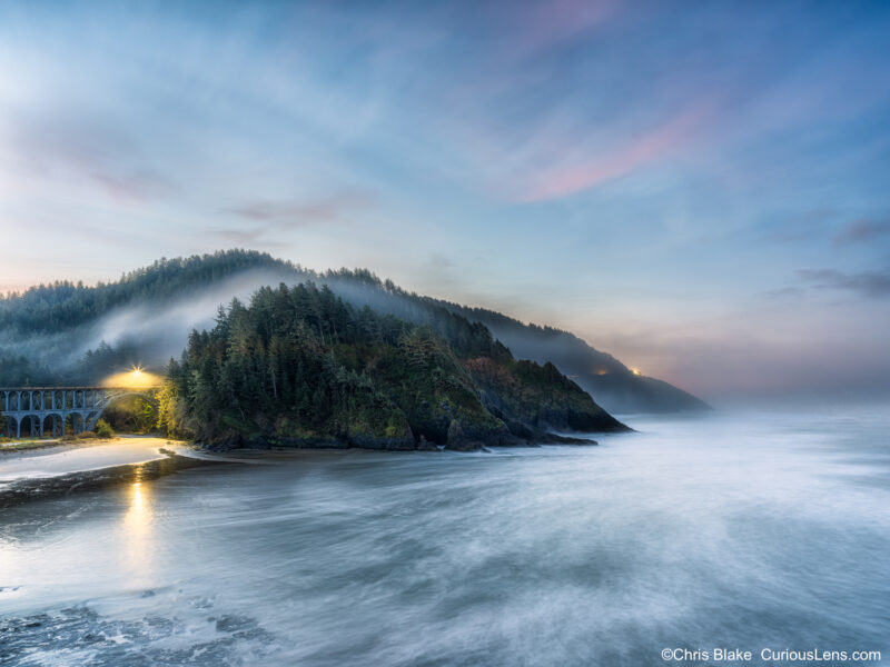Blue hour coastal scene at Heceta Head with moving water, low clouds, and a lit bridge