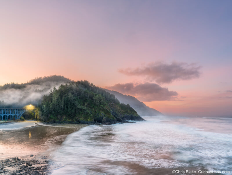 Sunrise at Heceta Head Lighthouse with pastel sky, moving water, low clouds, and a lit coastal bridge