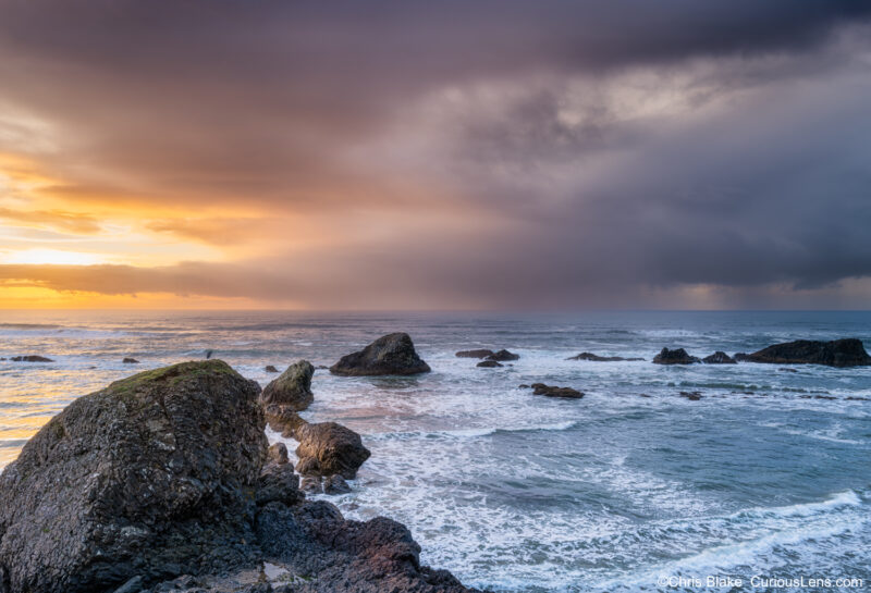Storm clouds moving over Seal Rock with sunset light fading and rain falling into the ocean