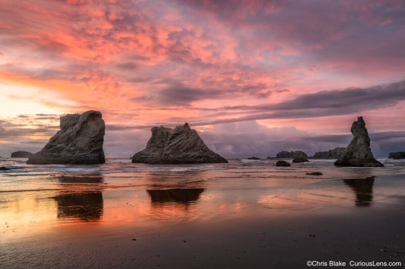 Sunset afterglow over the sea stacks at Bandon Beach on the Oregon Coast, with red clouds reflected in the wet sand.