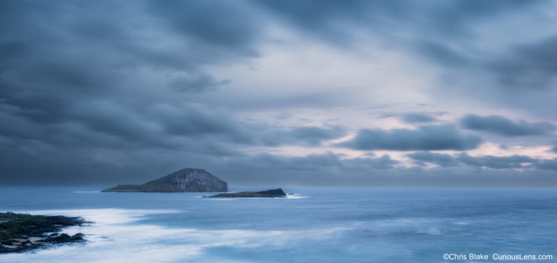 Moody blue hour sunrise over Kaohikaipu Island near Makapuʻu Lookout on Oahu, Hawaii, with storm clouds and a long exposure softening the ocean waves.
