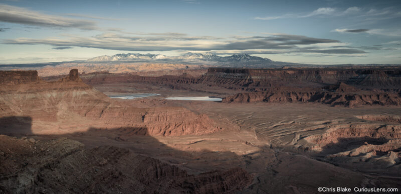 Late afternoon view from Dead Horse Point State Park in Utah, with deep desert shadows, the potash mine below, and snow-covered La Sal Mountains in the distance.