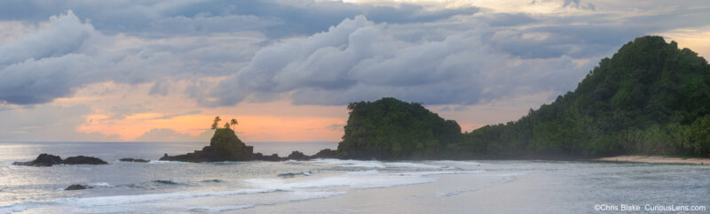 Large panoramic sunset photograph of the American Samoa coast, with volcanic rock formations, palm trees, ocean waves, and soft evening light over the South Pacific.