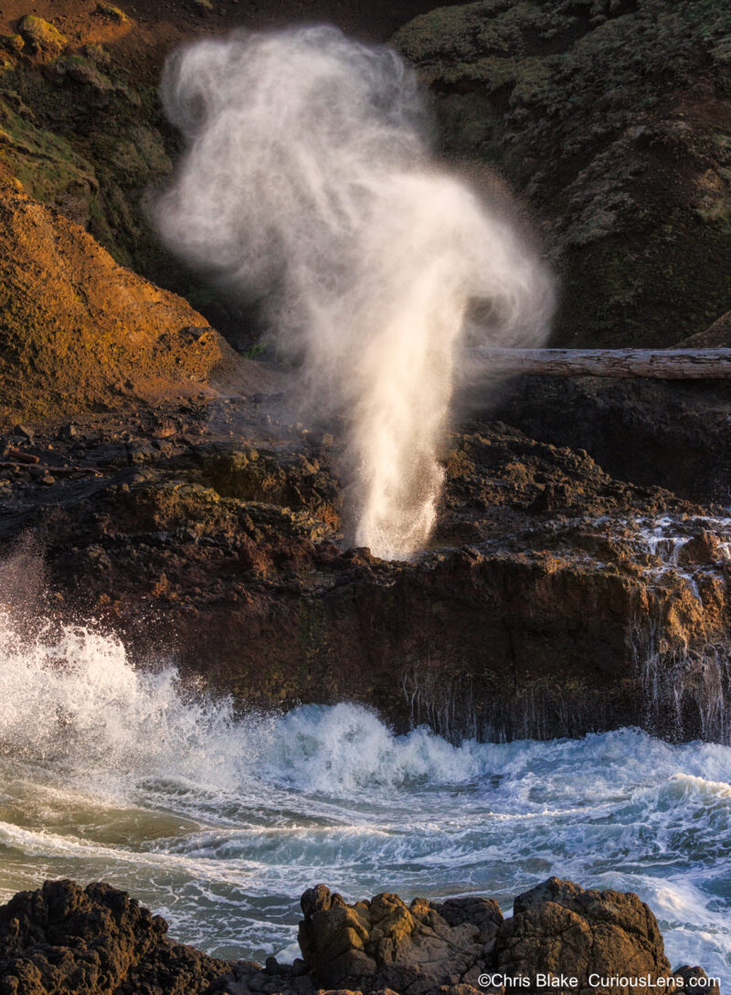 Ocean water exploding from the Spouting Horn at Cape Perpetua on the Oregon Coast, lit by warm late-day sunlight.